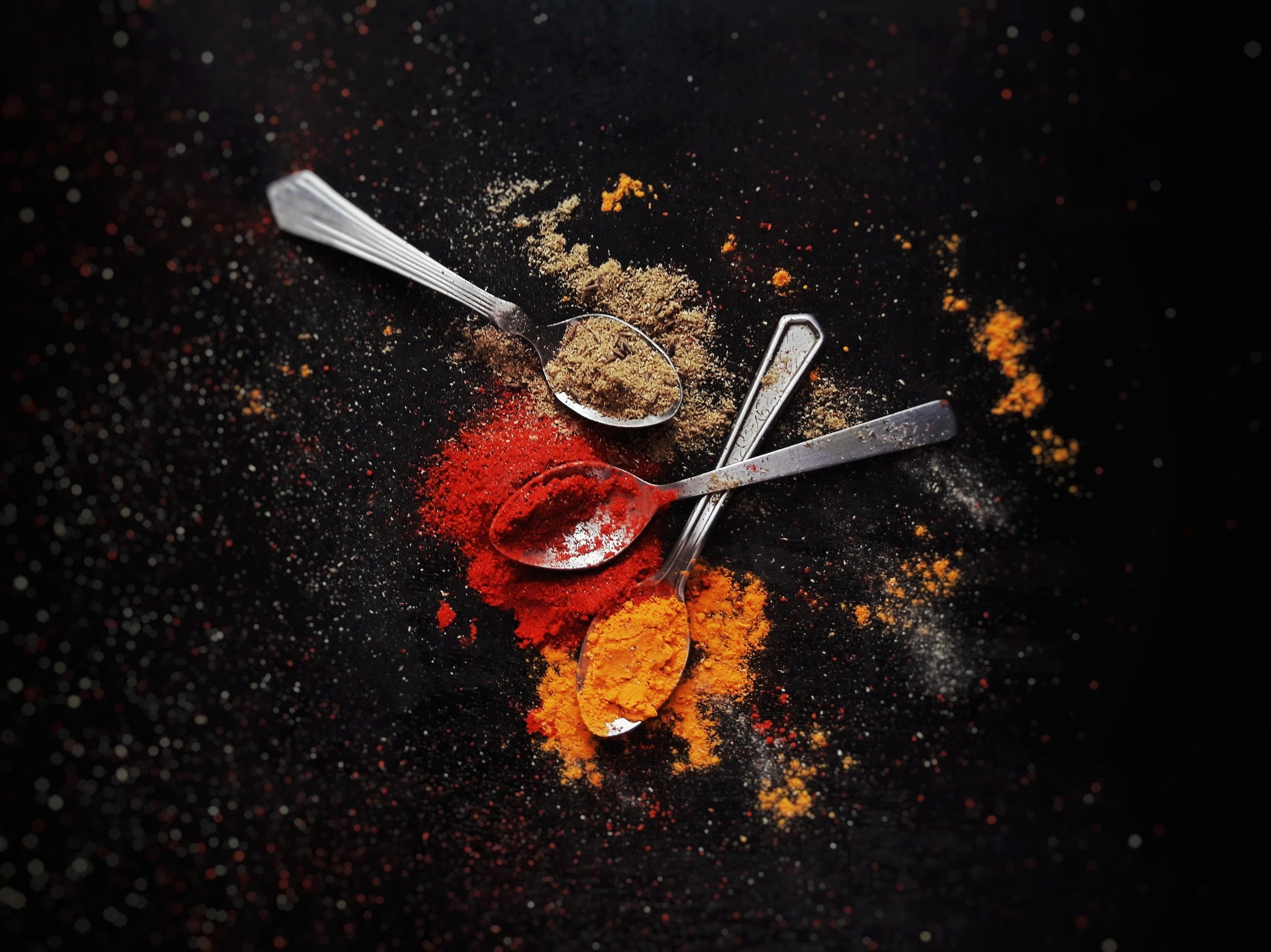 Spoons holding various colorful spices on a black background.